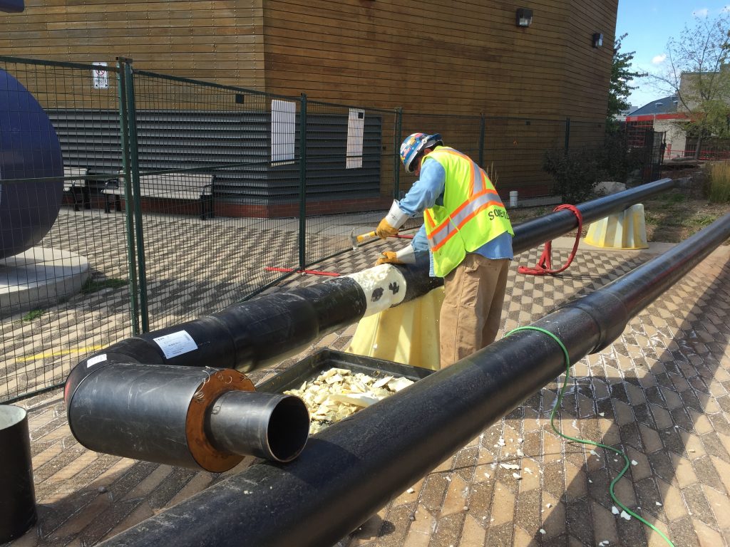 A construction worker hammers a large pipe, above ground.