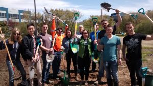Group of community garden members smiling, and raising their shovels above their heads.