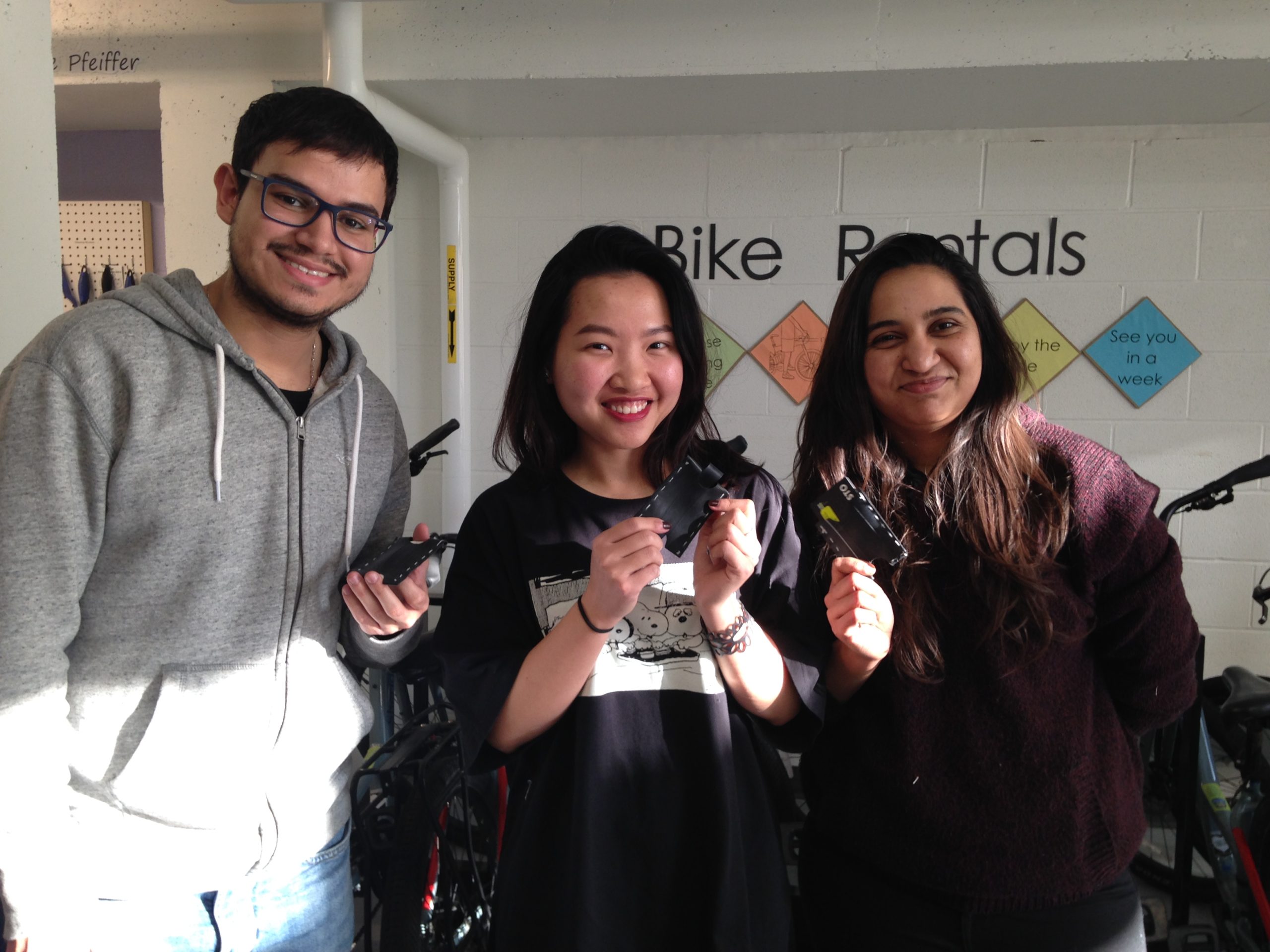 Three students standing together holding up their card holders and bracelet made with bike tubes.