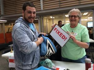 A repair cafe technician and student pose and smile for the camera. They have fixed the student's backpack.