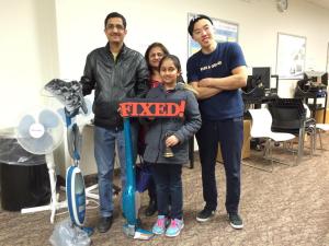 A man, woman, child, and a repair cafe technician pose for the camera, with their fixed vacuum cleaner.