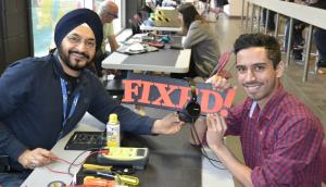 A repair café technician and a student pose and smile for the camera. They have fixed over-the-ear headphones.